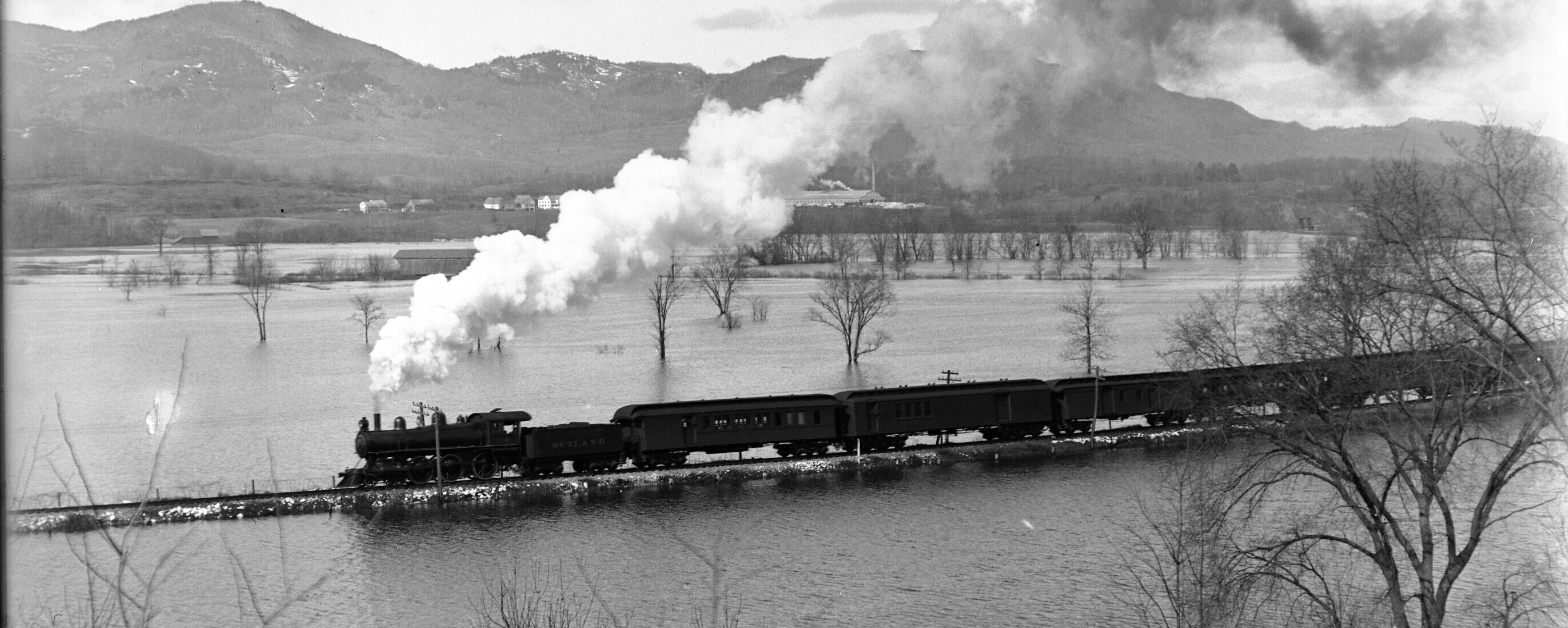 Black and white photo of a train traveling over tracks in flooded field