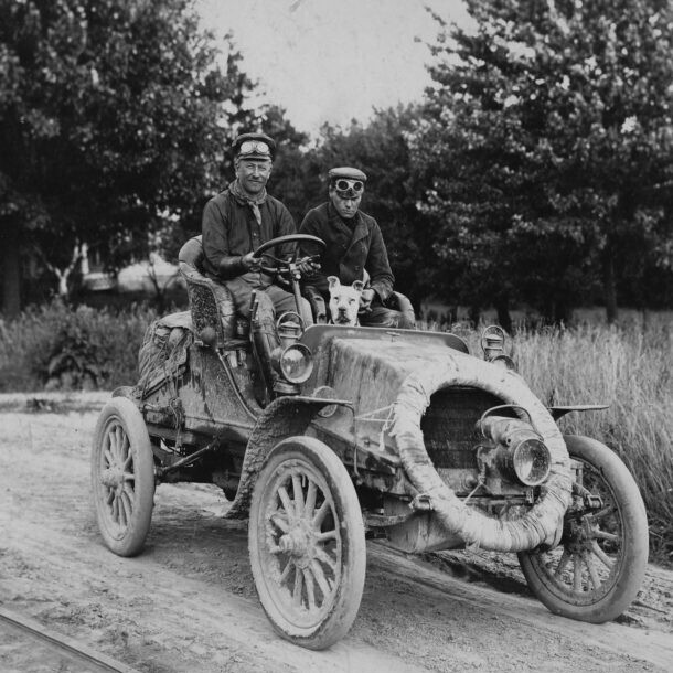 two men in old car with dog